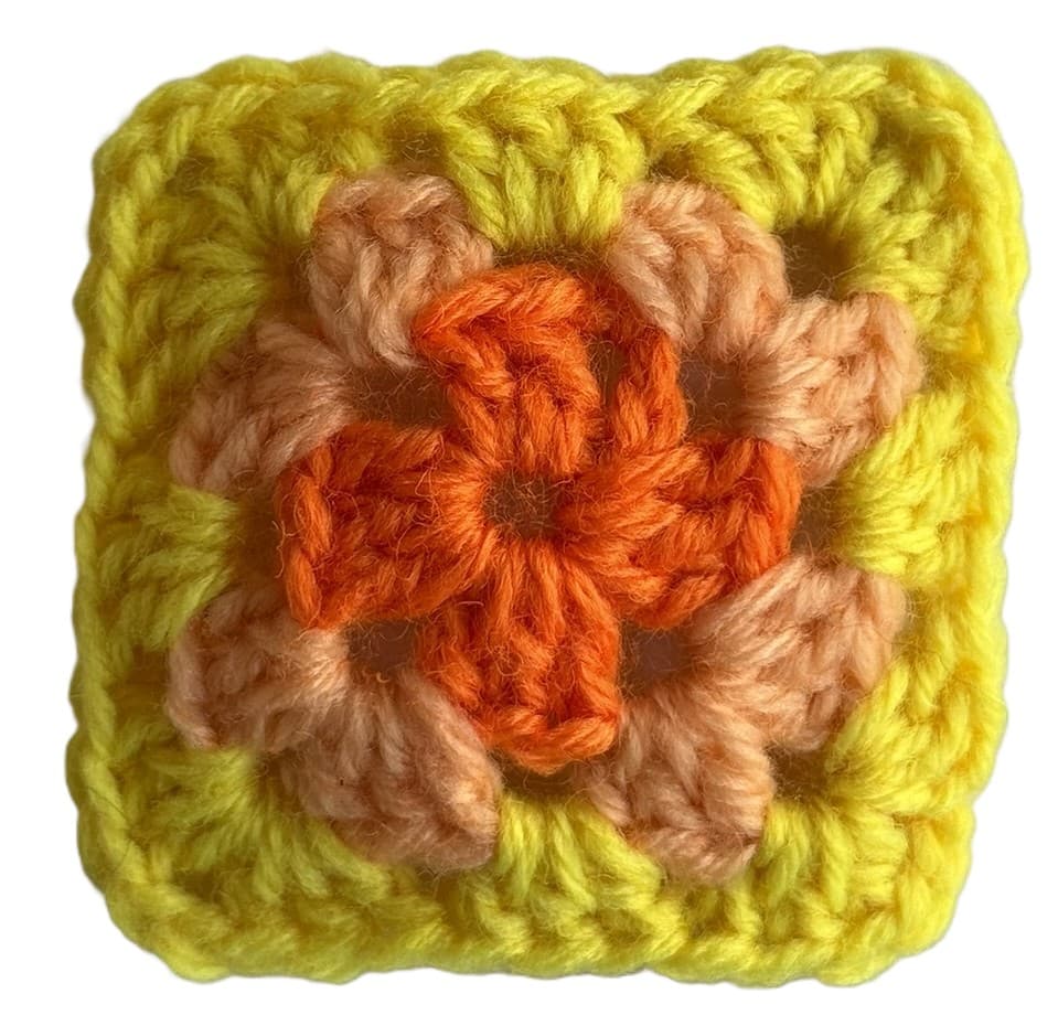 A handmade crochet granny square with a yellow and orange flower motif centered in the middle.