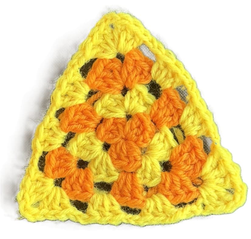 A handmade crochet granny triangle in yellow and orange, photographed flat on a wooden surface.