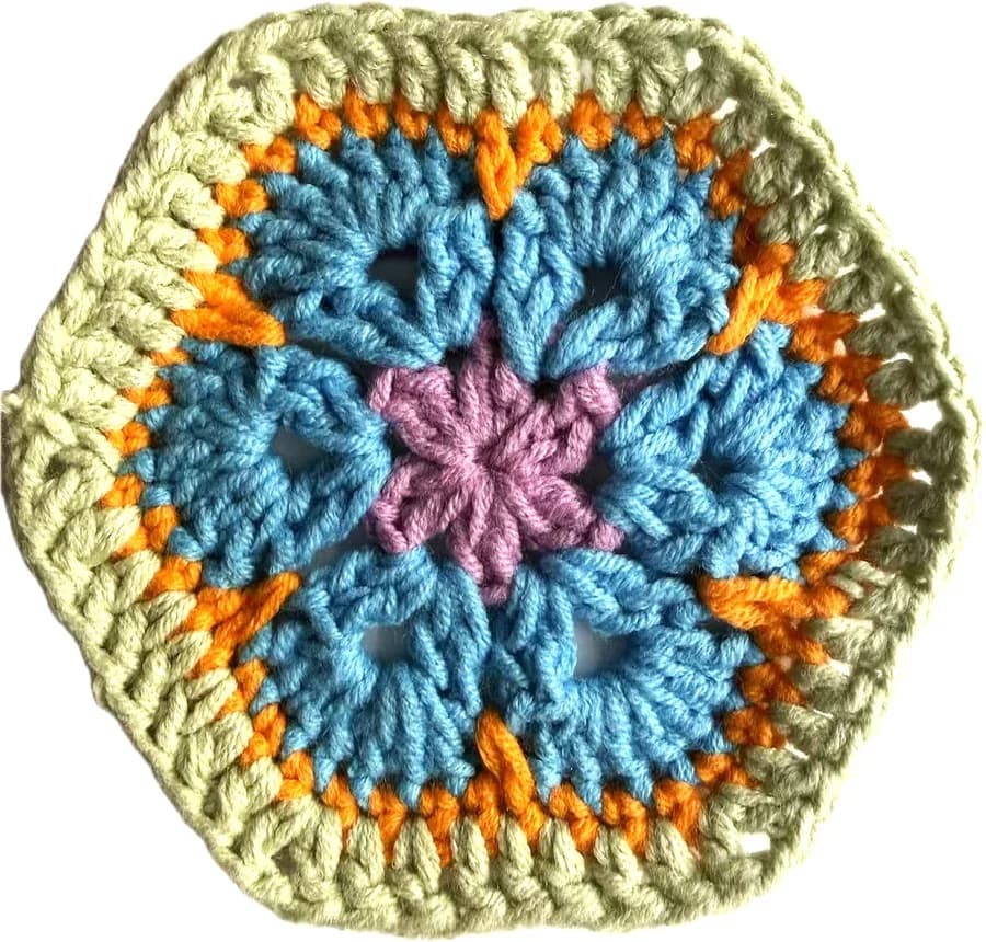A handmade African Flower hexagon crocheted in spring colors — pink center, blue petals, orange transition, sage green border.
