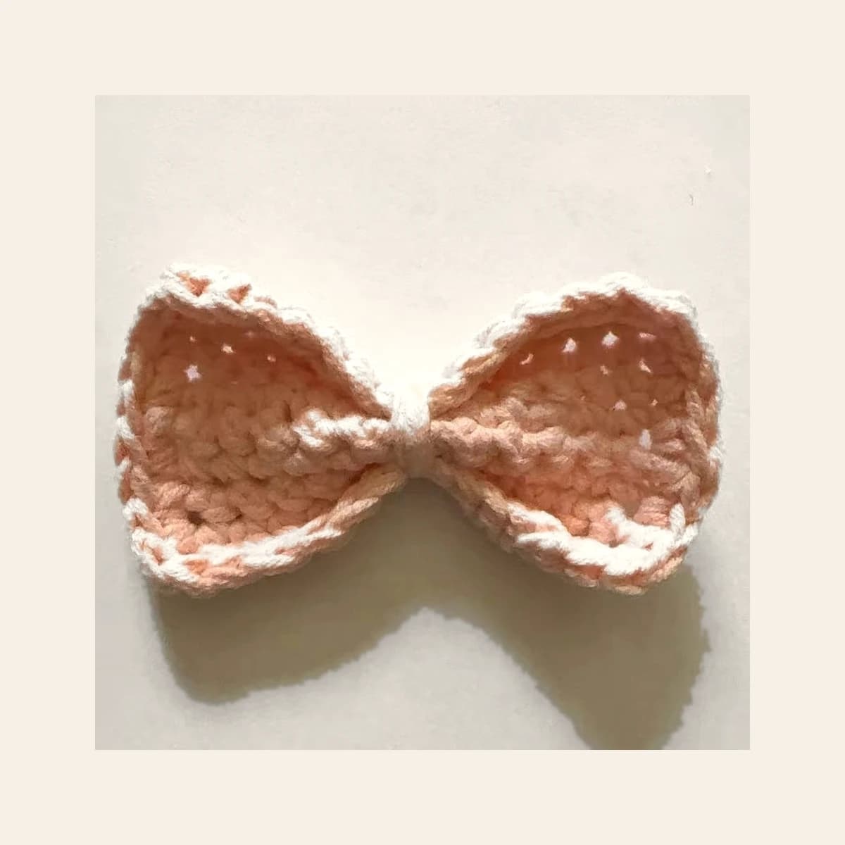 A crocheted bow sample photographed on a warm neutral background.