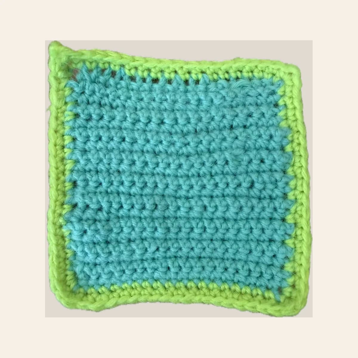 A turquoise crochet practice square with a bright green border on a warm neutral background.