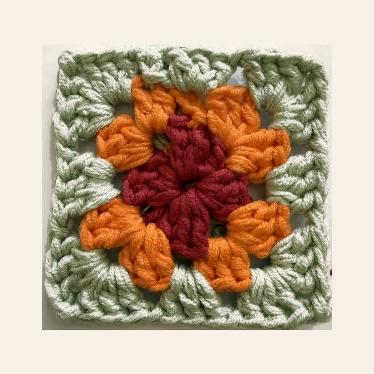 A crocheted floral granny square sample photographed on a warm neutral background.